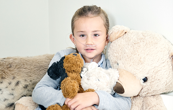 Mädchen mit Nasenbrille sitzt auf einem Sofa, umgeben von Plüschtieren